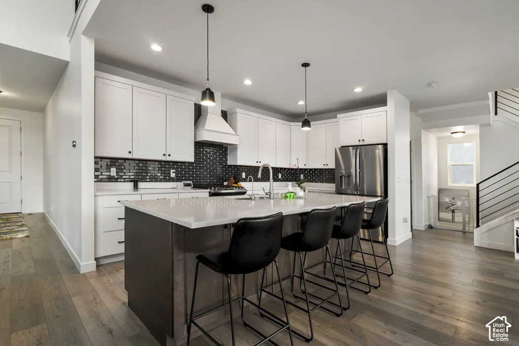 Kitchen featuring a central island with a solid surface countertop, white shaker-style cabinetry, dark tile backsplash, stainless steel appliances, and wood-finish flooring