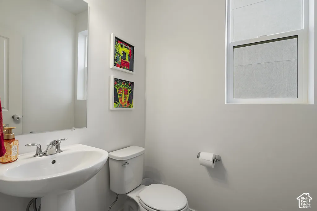 White pedestal sink with chrome dual-handle faucet, large wall-mounted mirror, single-flush toilet, and operable window with white casing