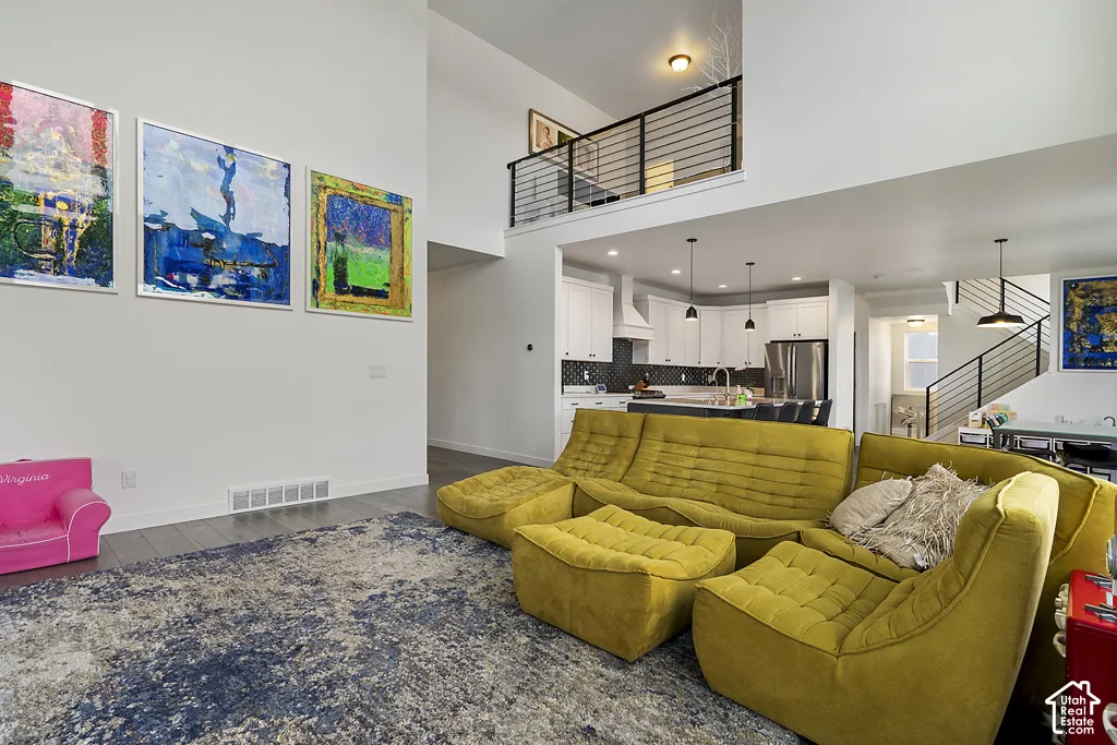 Open-concept interior featuring double-height ceilings, a mezzanine balcony with metal railings, white cabinetry, and wood-finish flooring