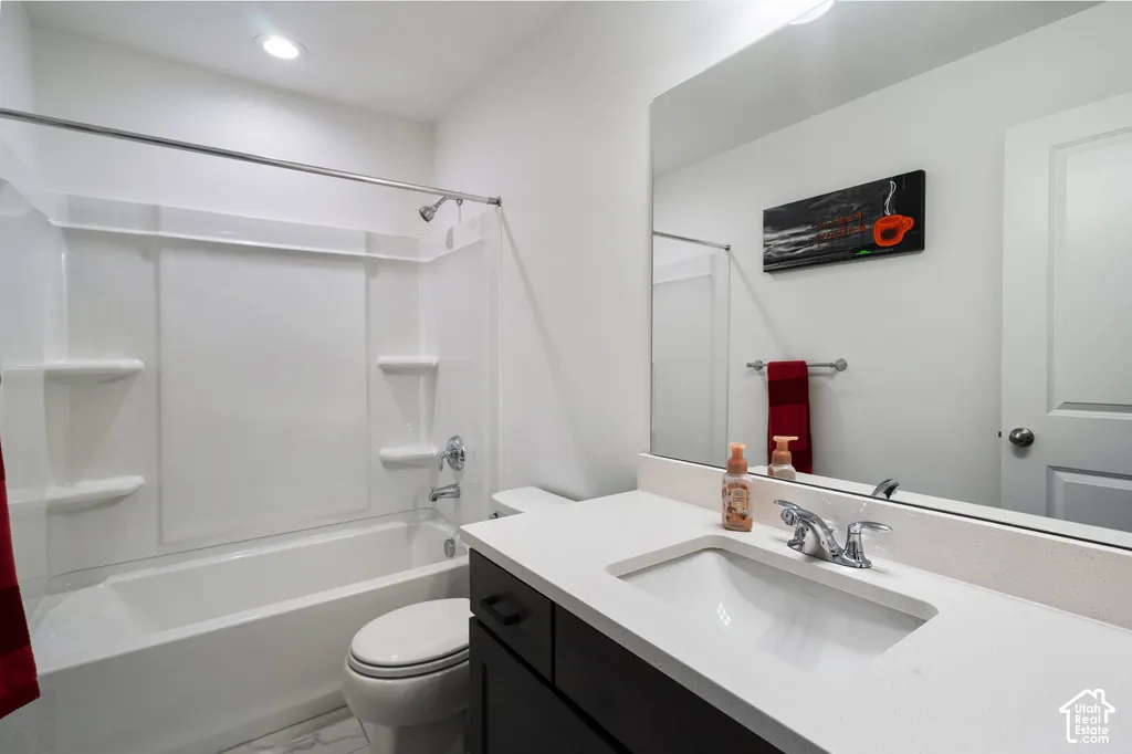 Bathroom featuring a dark-finish vanity with a stone-surface countertop, an integrated sink, an expansive wall-mounted mirror, and a tub-shower combination with built-in shelving