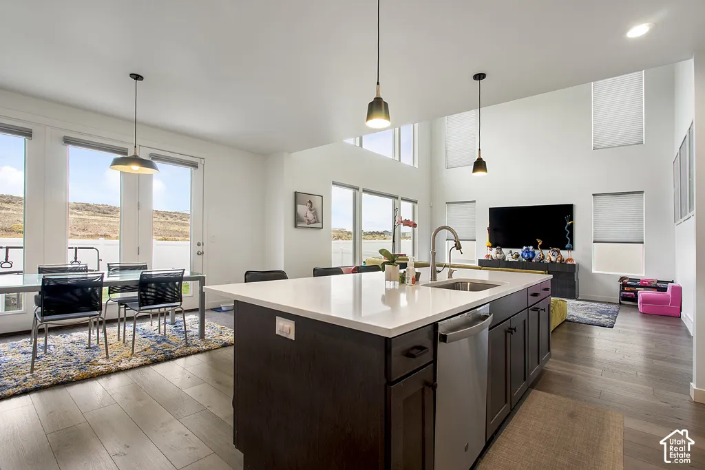 Center kitchen island with quartz countertop and undermount sink, dark-stained cabinetry, wood-finish flooring, soaring ceilings, and expansive windows