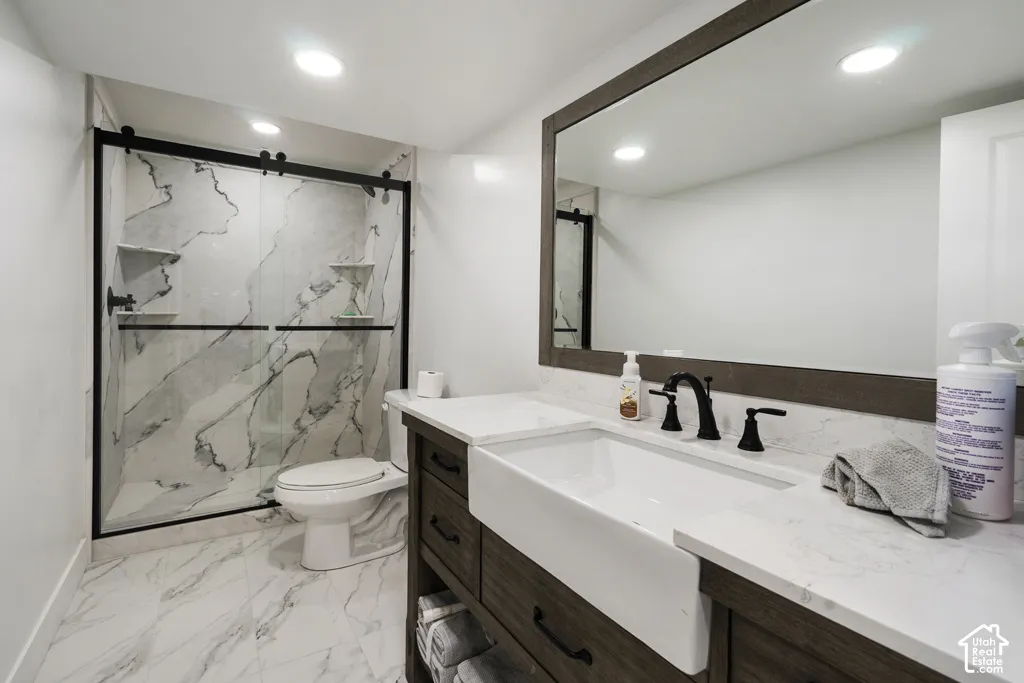 Bathroom featuring a farmhouse-style apron sink, custom wood-finish vanity with stone-look countertop, large-format stone-look tile flooring, and a walk-in shower with matte black sliding glass doors