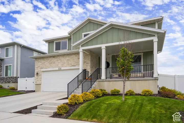 Two-story exterior featuring board and batten siding, natural stone facade, attached two-car garage, concrete driveway, and covered front porch with metal railing