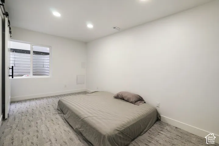 Neutral-toned wall-to-wall carpeting, recessed ceiling lighting, and a sliding barn-style door
