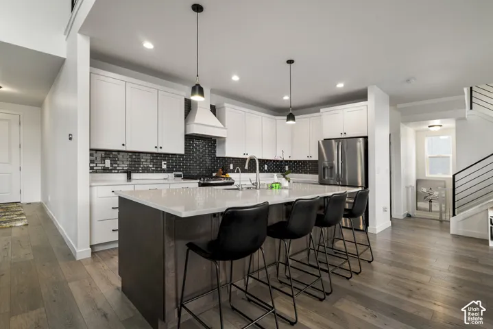 Kitchen featuring a central island with a solid surface countertop, white shaker-style cabinetry, dark tile backsplash, stainless steel appliances, and wood-finish flooring