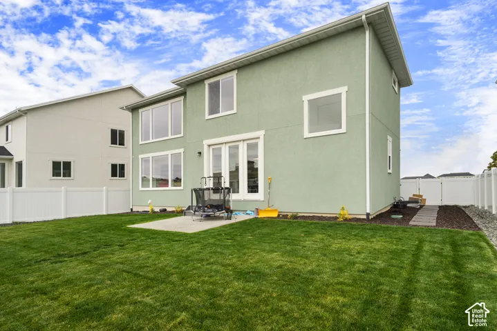 Rear exterior featuring stucco siding, large windows with white trim, double French doors, a concrete patio, and white vinyl perimeter fencing