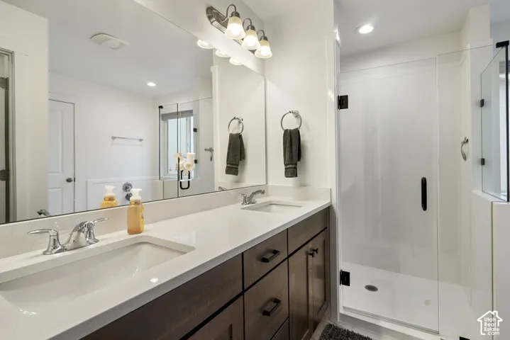 Double vanity with a stone countertop, under-mount sinks, dark-finish cabinetry, and a glass-enclosed shower