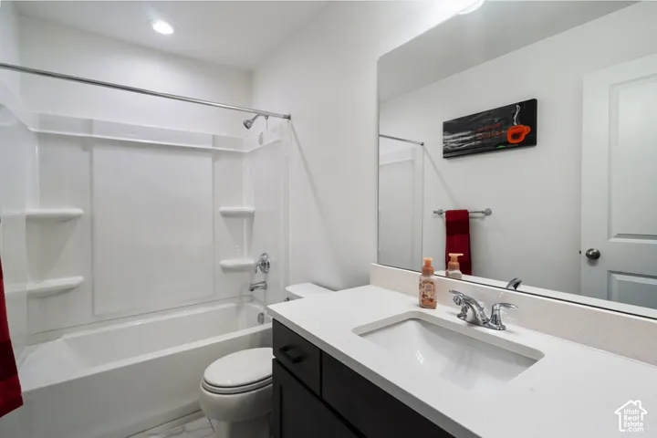Bathroom featuring a dark-finish vanity with a stone-surface countertop, an integrated sink, an expansive wall-mounted mirror, and a tub-shower combination with built-in shelving