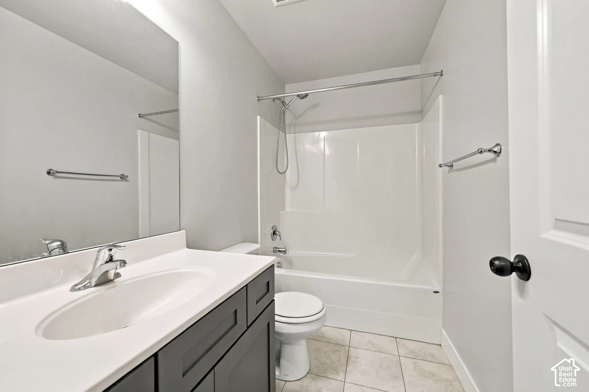 Dark gray vanity cabinet with a white countertop and integrated sink, large wall-mounted mirror, ceramic tile flooring, and a tub-shower combination with a chrome fixture