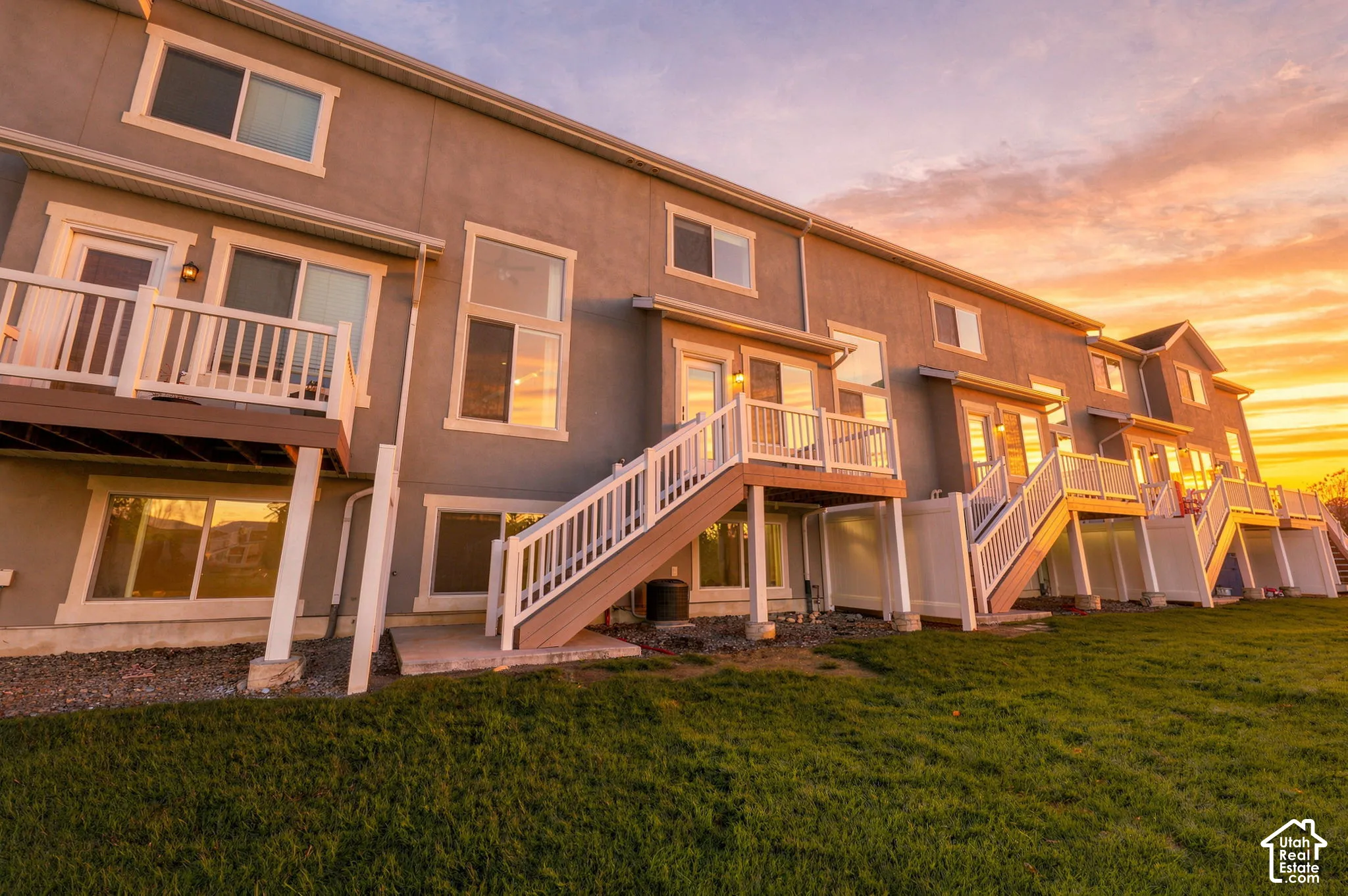 Stucco exterior featuring elevated decks with white railings, ground-level entryways, and large windows