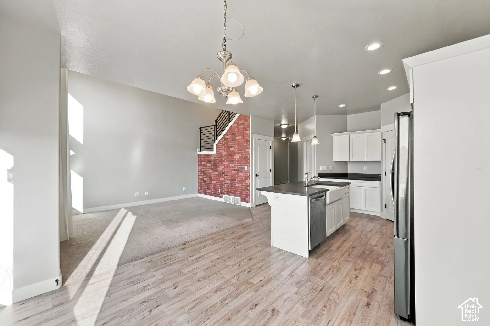 Kitchen featuring white cabinetry, dark countertops, an apron-front sink, and wood-finish flooring, accented by an interior brick feature wall and multi-light hanging fixtures