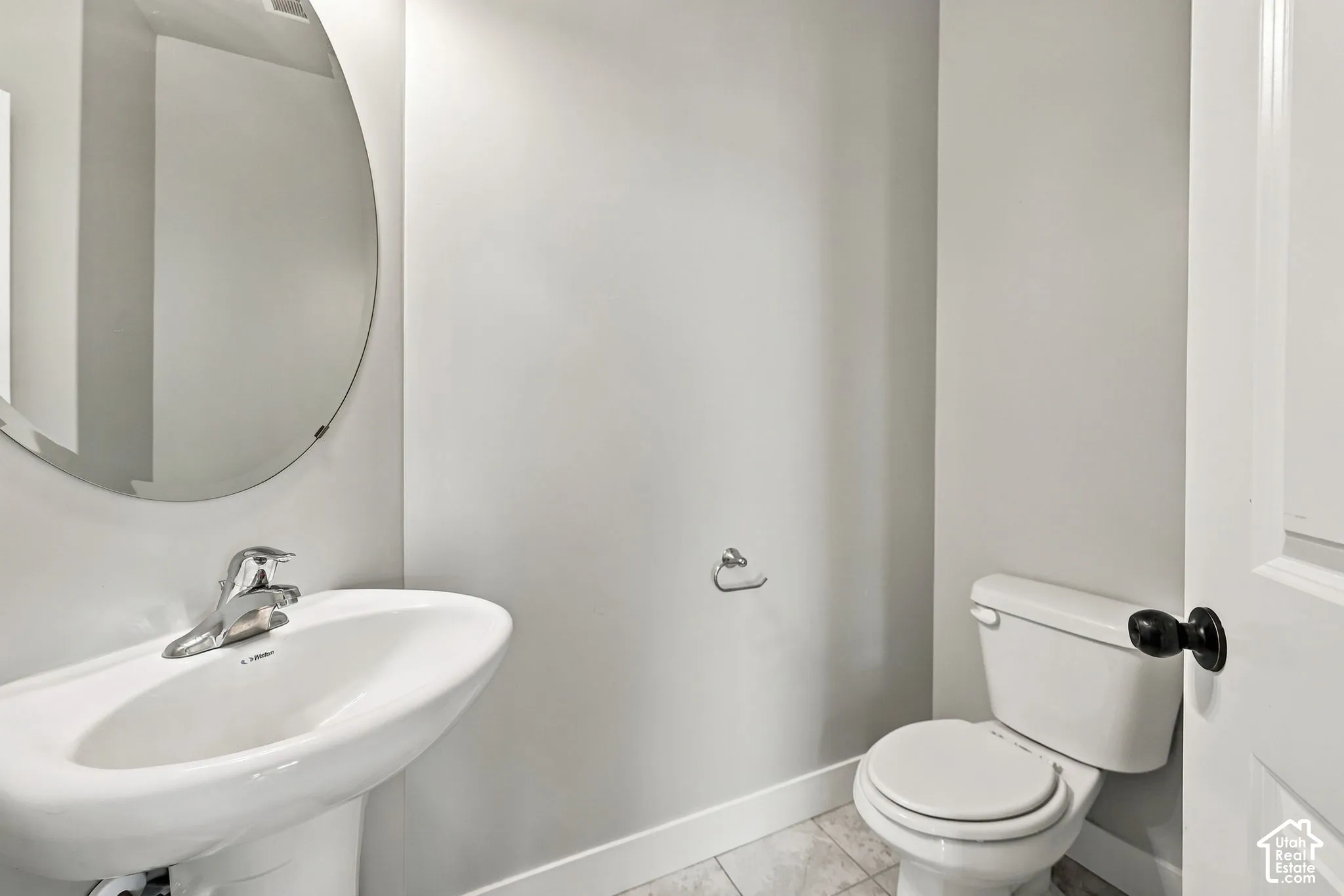 Wall-mounted oval mirror, white pedestal sink with chrome faucet, and tile flooring