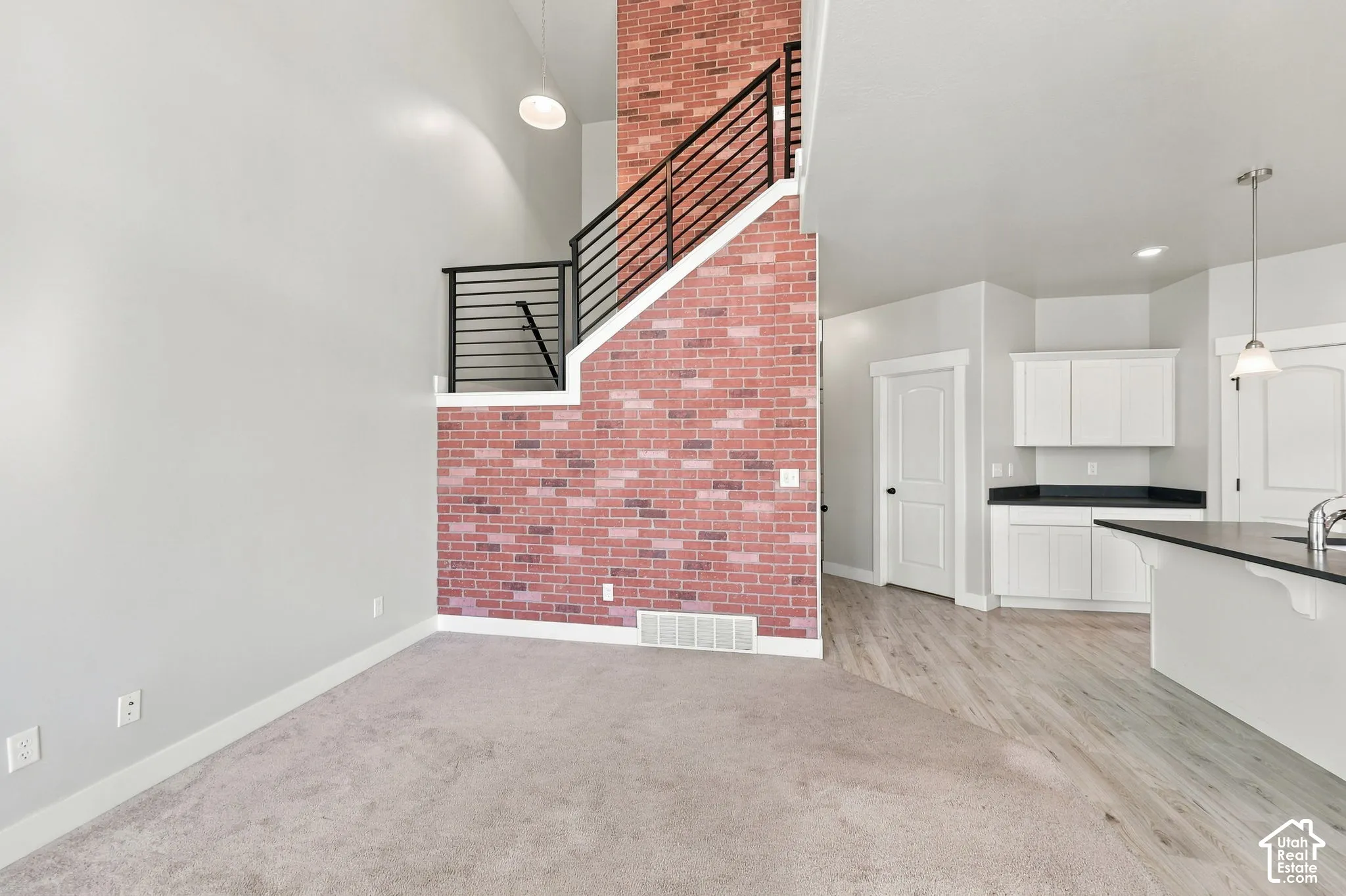 Full-height brick feature wall, metal horizontal baluster railing, vaulted ceilings, and white shaker-style cabinetry with dark countertops