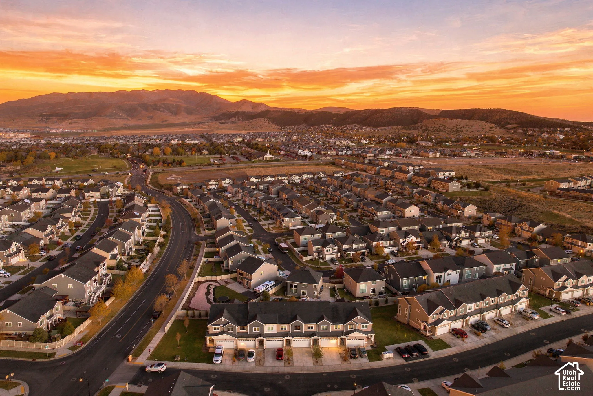 Aerial perspective featuring a multi-unit residential structure with asphalt shingle roofing, paved driveways, and mountain range backdrop