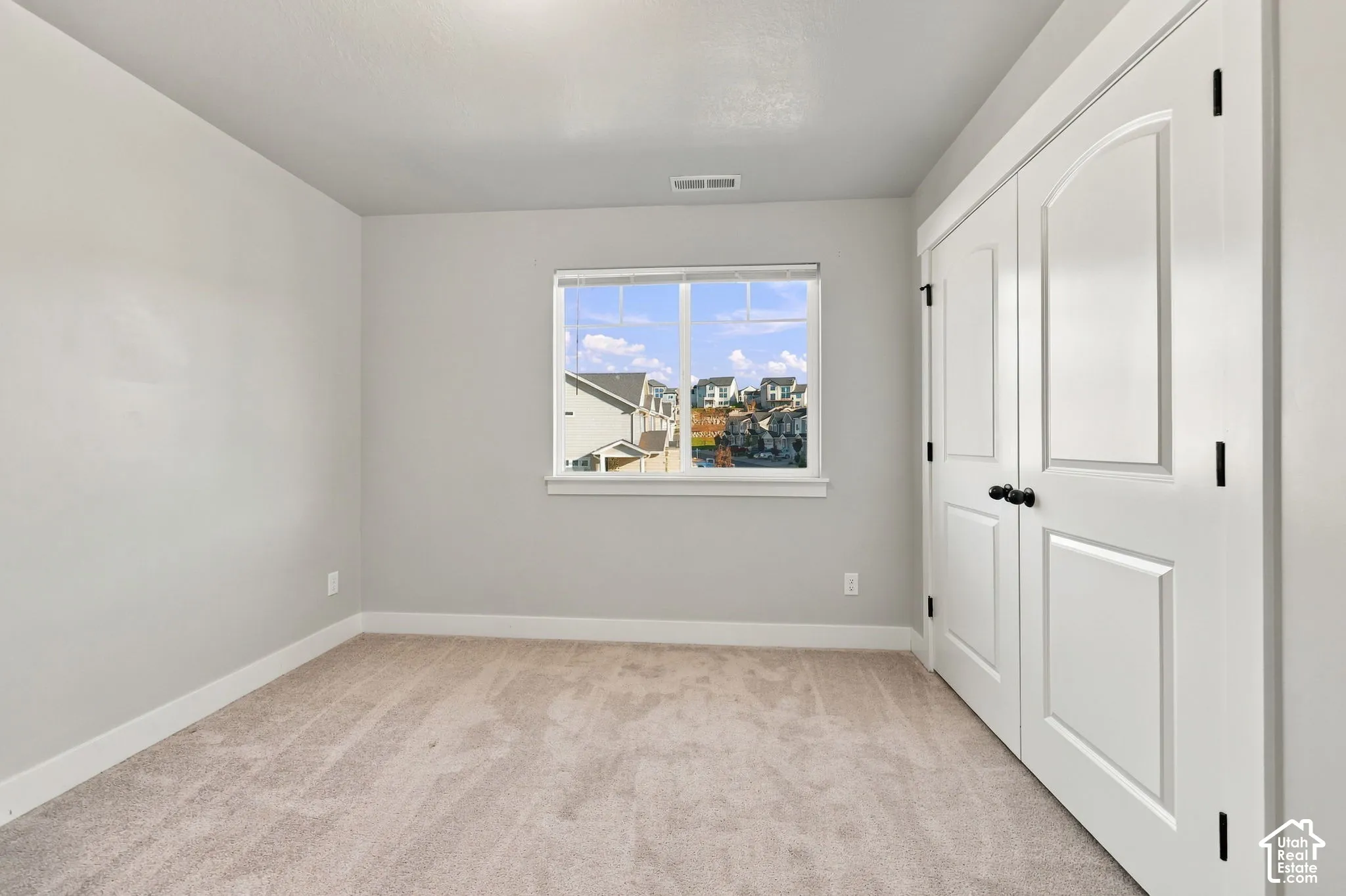 Room featuring neutral carpeting, light-toned wall paint, a single-hung window, and white double-panel doors with black hardware