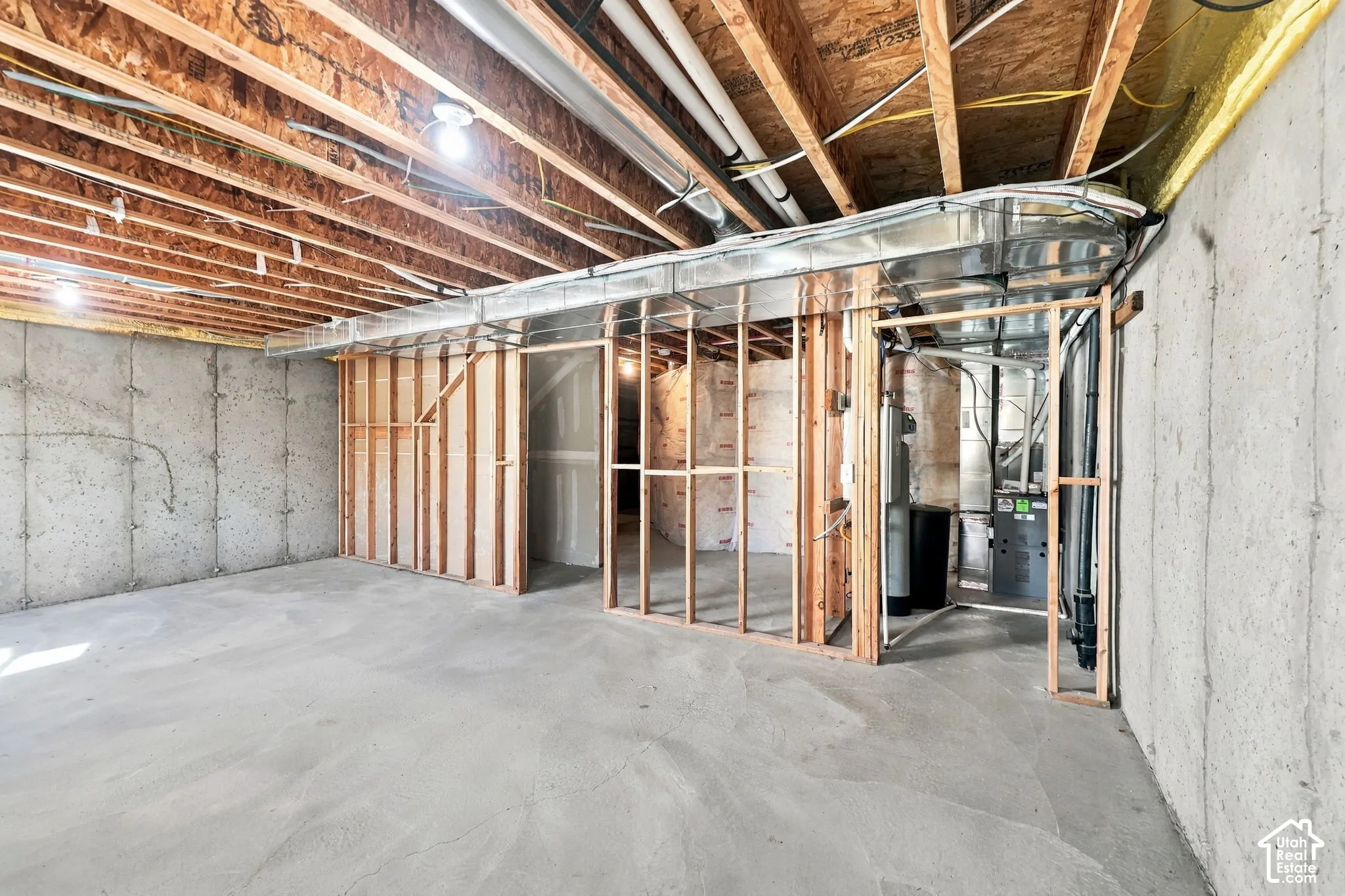 Unfinished basement featuring exposed wood-joist ceiling, concrete foundation walls, stud-framed partitions, and an exposed HVAC system