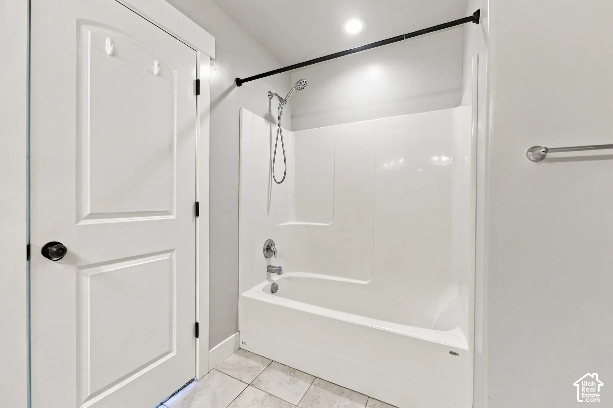 Full-height white shower surround with integrated tub, handheld shower fixture, matte black shower rod, and tiled flooring