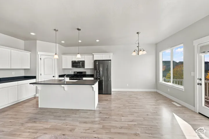 Kitchen featuring white cabinetry, dark countertops, an island with an undermount sink, pendant lighting, and wood-finish flooring