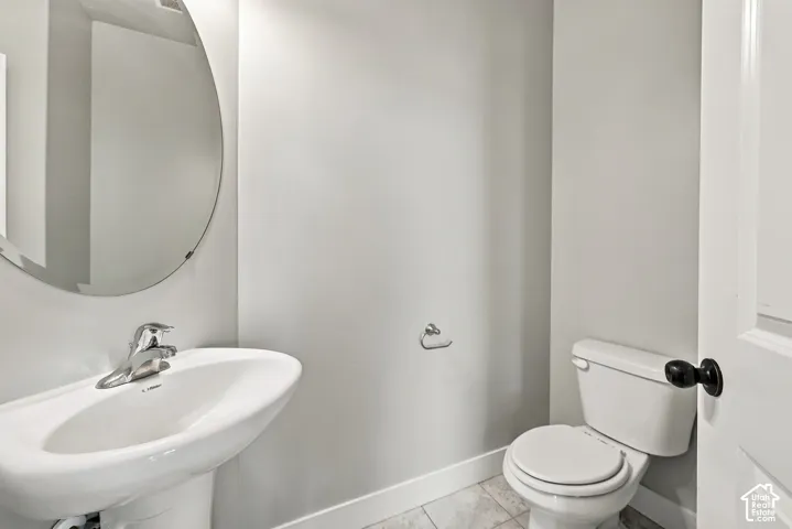 Wall-mounted oval mirror, white pedestal sink with chrome faucet, and tile flooring