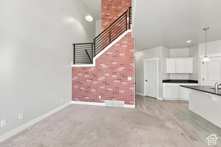 Full-height brick feature wall, metal horizontal baluster railing, vaulted ceilings, and white shaker-style cabinetry with dark countertops
