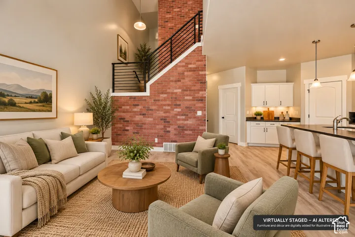 Open-concept interior featuring a floor-to-ceiling red brick accent wall, staircase with matte black metal railings, wood-finish flooring, and white kitchen cabinetry with dark countertops