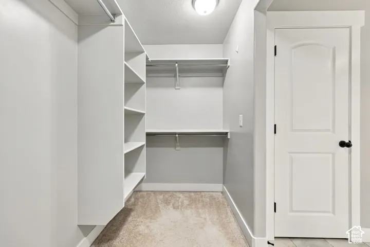 Walk-in closet featuring white built-in shelving, dual-tier metal rods, carpeted flooring, and a solid-core panel door with matte black hardware