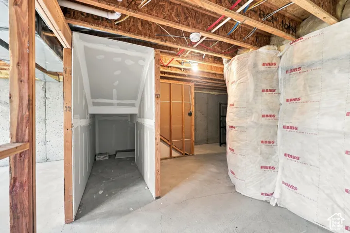 Unfinished lower-level space featuring concrete foundation walls, partially installed drywall framing, exposed wood-joist ceiling, and thermal insulation wrap