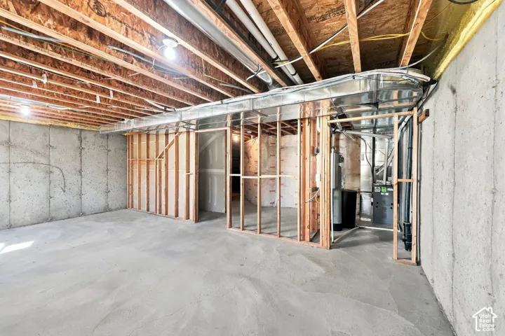 Unfinished basement featuring exposed wood-joist ceiling, concrete foundation walls, stud-framed partitions, and an exposed HVAC system