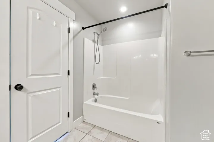 Full-height white shower surround with integrated tub, handheld shower fixture, matte black shower rod, and tiled flooring