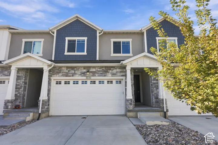 Two-story townhome exterior featuring stone veneer accents, shake siding, white columns, and a multi-car garage