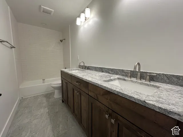 Bathroom featuring a dual-sink vanity with stone countertop, wood-finish cabinetry, tile flooring, and a bathtub with white tile surround