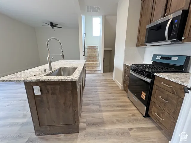 Kitchen featuring stained wood cabinetry, stone-patterned countertops, a stainless steel undermount sink with an arched pull-down faucet, and wood-finish flooring
