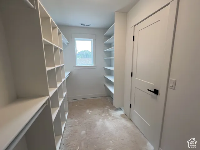 Walk-in closet featuring white built-in shelving, a single-hung window with casing, and a shaker-style interior door with matte black hardware