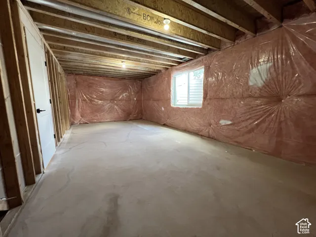 Unfinished interior space featuring exposed engineered wood joists, concrete flooring, vapor-barrier-wrapped walls, and a recessed window