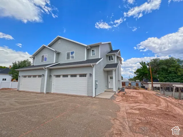 Multi-story exterior featuring light gray horizontal siding, dual two-car garages, and an asphalt-shingle roof