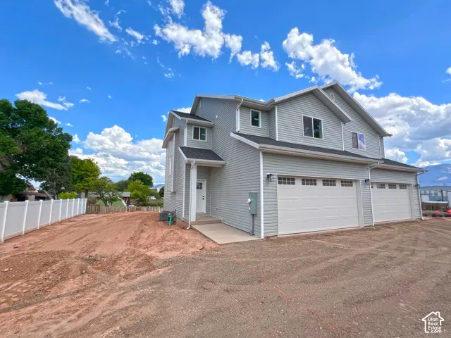 Two-story residence featuring light gray horizontal siding, a multi-car garage with overhead paneled doors, and a white privacy fence
