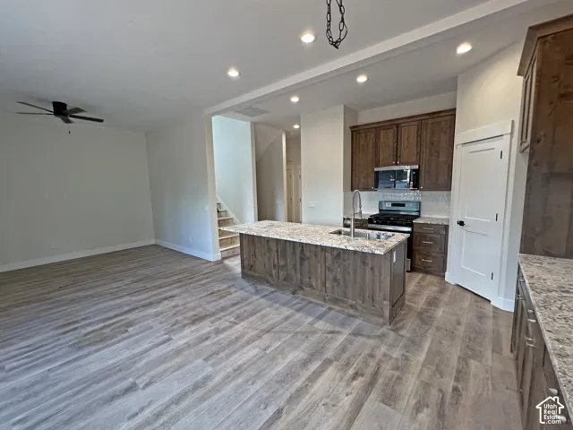 Kitchen featuring wood-finish cabinetry, stone-surface countertops, a center island with an integrated sink, and wood-finish flooring
