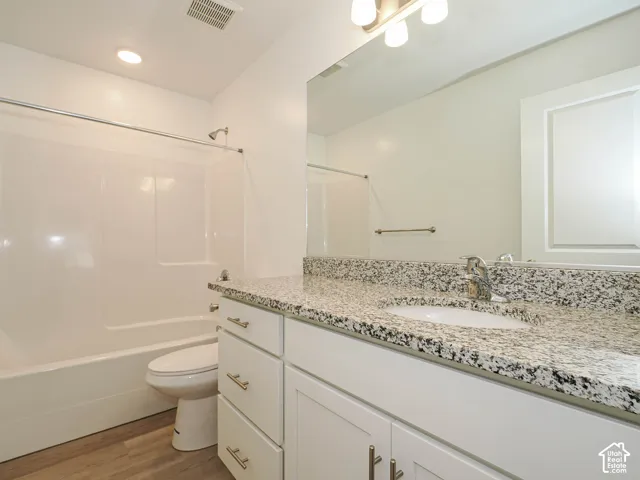 Bathroom featuring a white vanity with stone-patterned countertop, an integrated sink, polished metal hardware, and a tub-shower combination with full-height wall surround