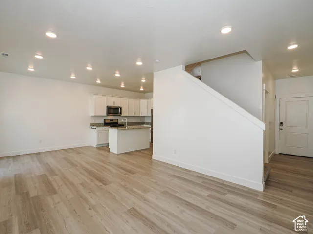Open floor plan featuring wood-finish flooring, recessed lighting, white cabinetry, and a kitchen island with stone-surface countertops