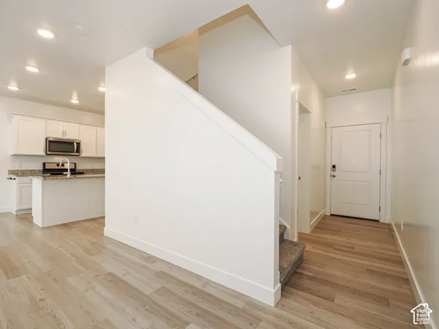 Entryway featuring wood-finish flooring, recessed lighting, and a paneled front door, including a kitchen area with white cabinetry, stone-surface countertops, and a stainless steel microwave