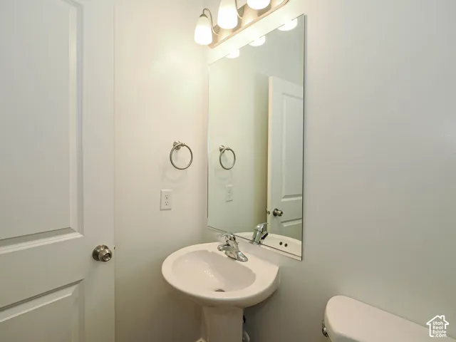 Pedestal sink featuring a polished chrome faucet, large wall-mounted mirror, and multi-bulb vanity light fixture