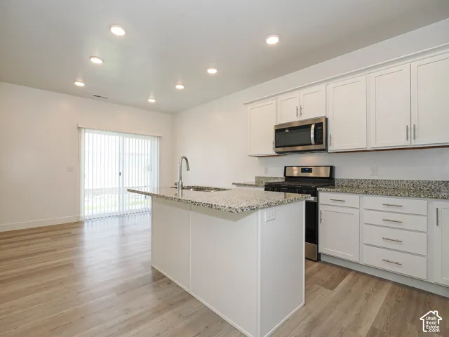 Kitchen featuring white cabinetry, stone-surface countertops, center island, stainless steel appliances, and wood-finish flooring