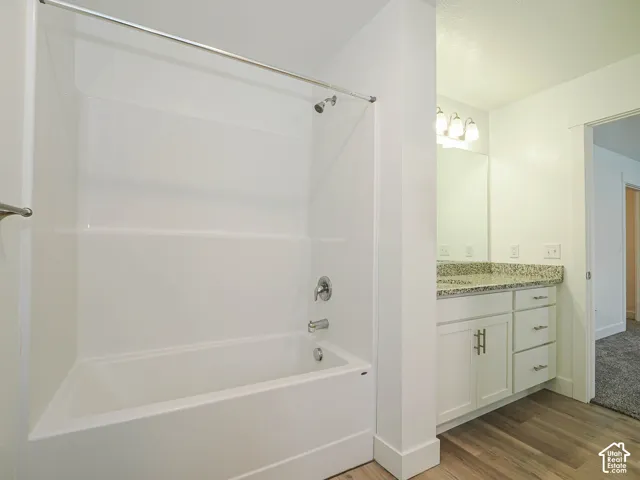 Bathroom featuring a white tub-shower combination, vanity with stone-surface countertop, integrated basin, cabinetry with metal hardware, and wood-finish flooring