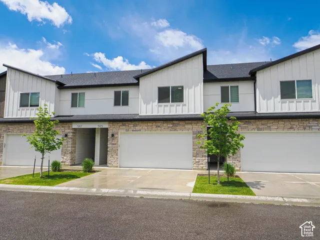 Modern townhouse exterior featuring vertical board-and-batten siding, natural stone veneer accents, integrated multi-car garages, and asphalt shingle roofing