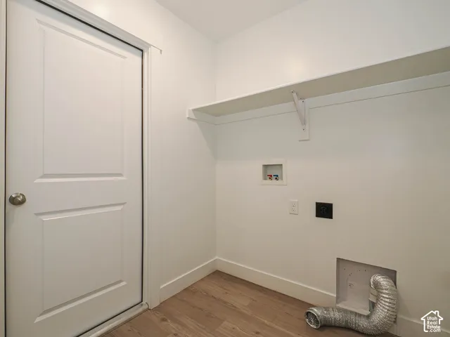 Utility space featuring wood-finish flooring, a white paneled door, a built-in overhead shelf, and dedicated washer and dryer hookups