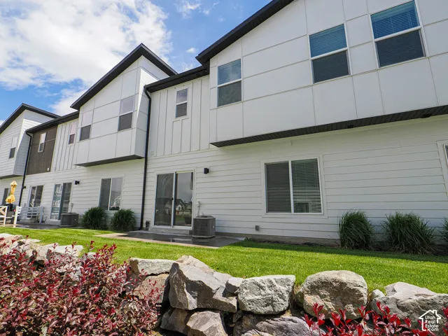 Exterior featuring white vertical and horizontal siding, multi-gabled roofline, sliding glass door, and tiered natural stone retaining wall landscaping