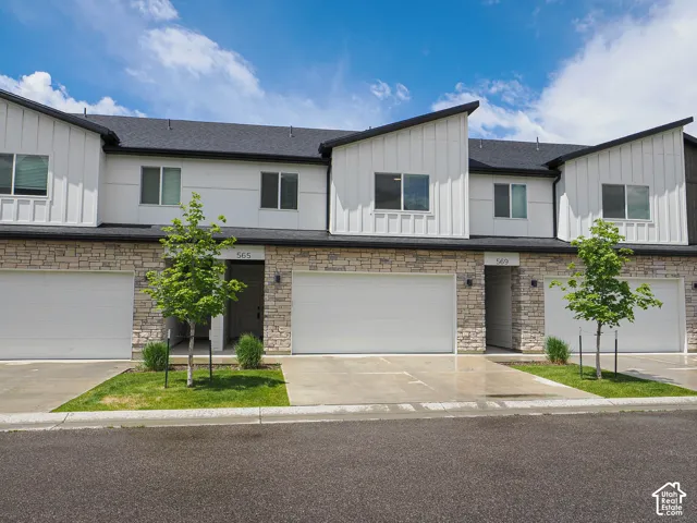 Modern townhome exterior featuring white vertical board-and-batten siding, natural stone veneer accents, multi-level shed rooflines, and private attached garages