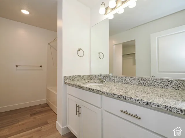 Vanity with stone-finish countertop, undermount sink, white cabinetry with metallic hardware, large wall mirror, and wood-finish flooring