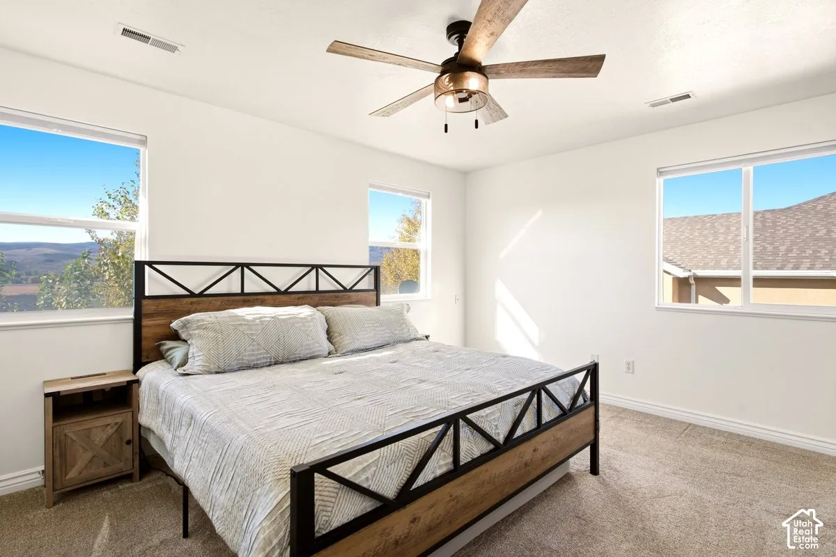 Neutral-toned carpeting, three large windows, and a ceiling fan with integrated lighting