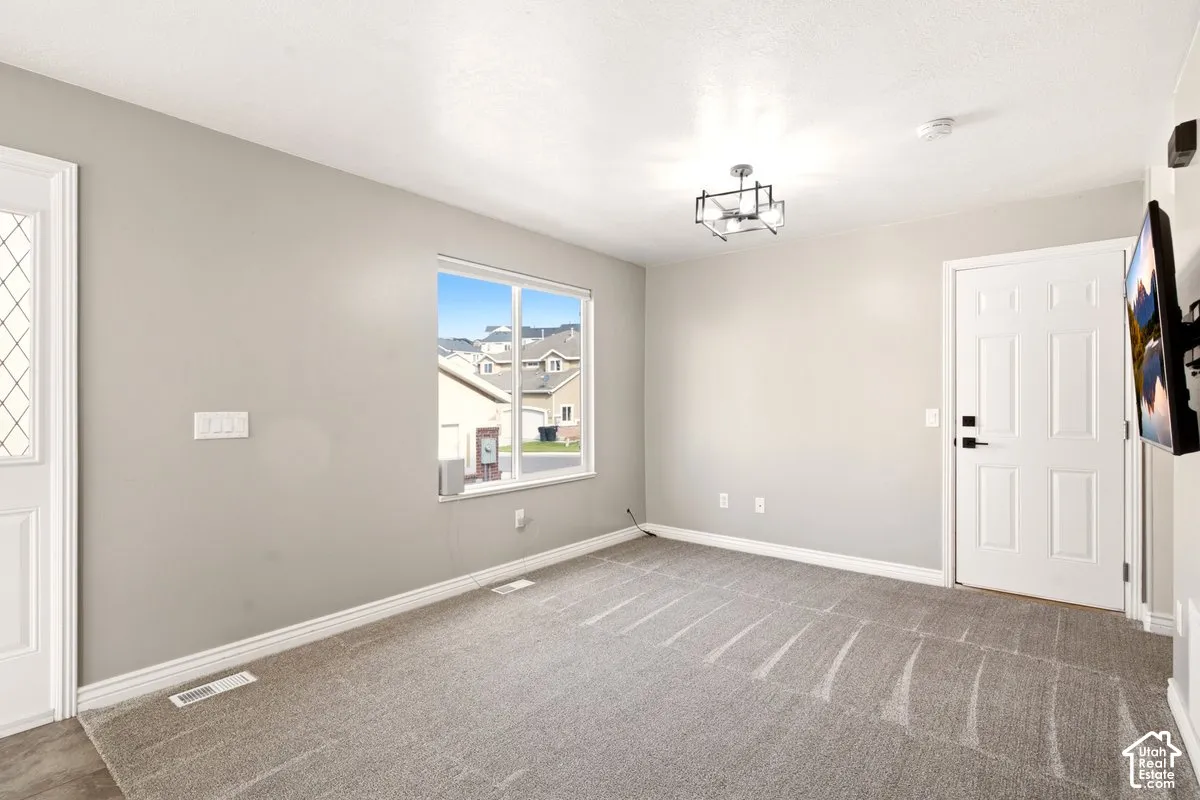 Neutral interior room featuring neutral-toned carpeting, a large picture window, a six-panel door, and a geometric chandelier